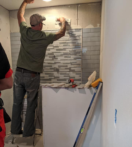 A man is installing a tile wall in a kitchen.