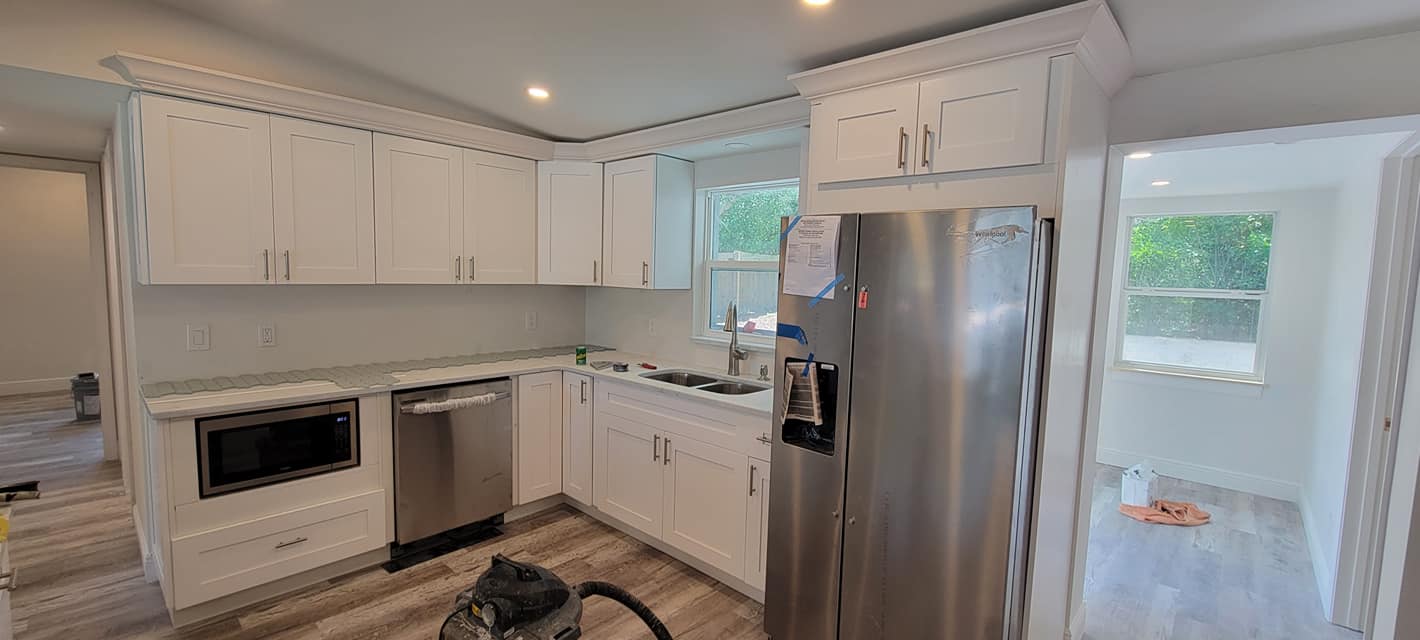 A kitchen with white cabinets , stainless steel appliances and a vacuum cleaner.