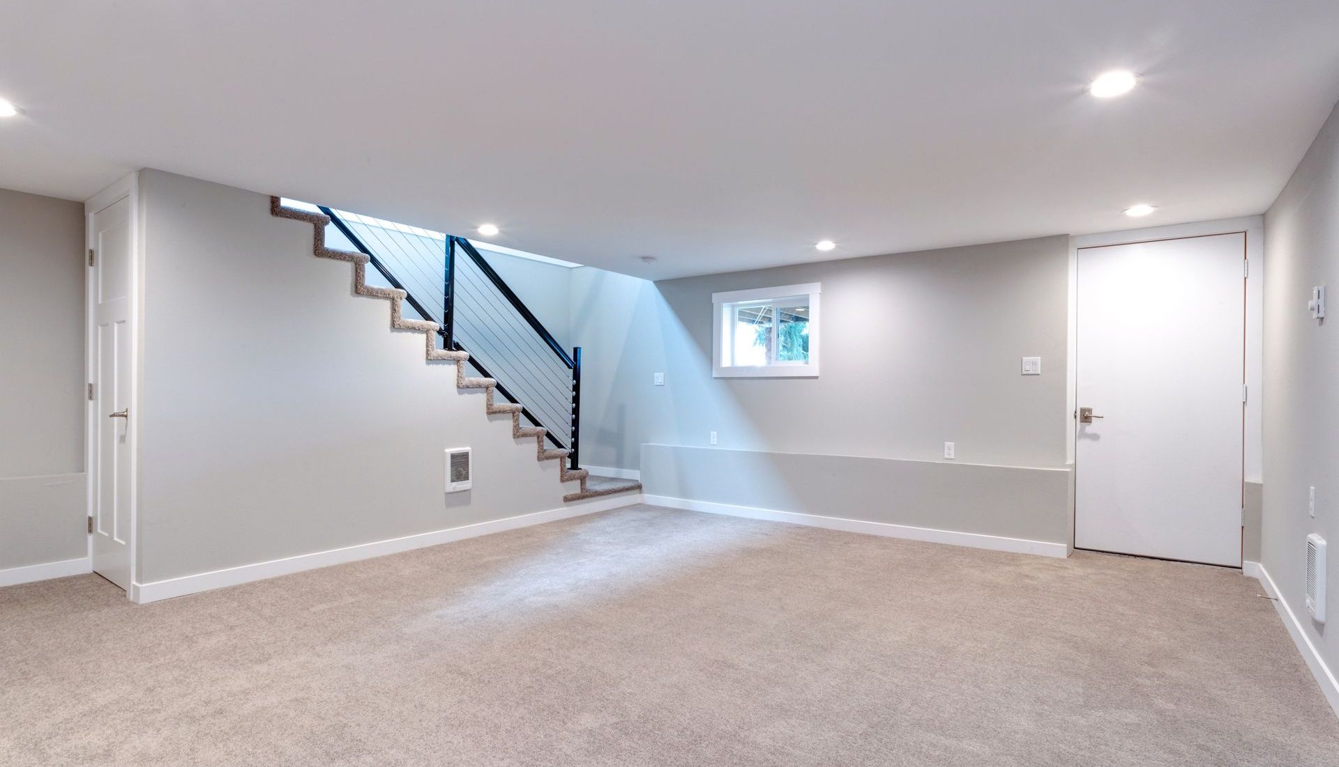 An empty basement with a staircase and a window.