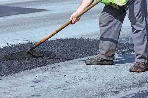 A man is spreading asphalt on the ground with a rake.