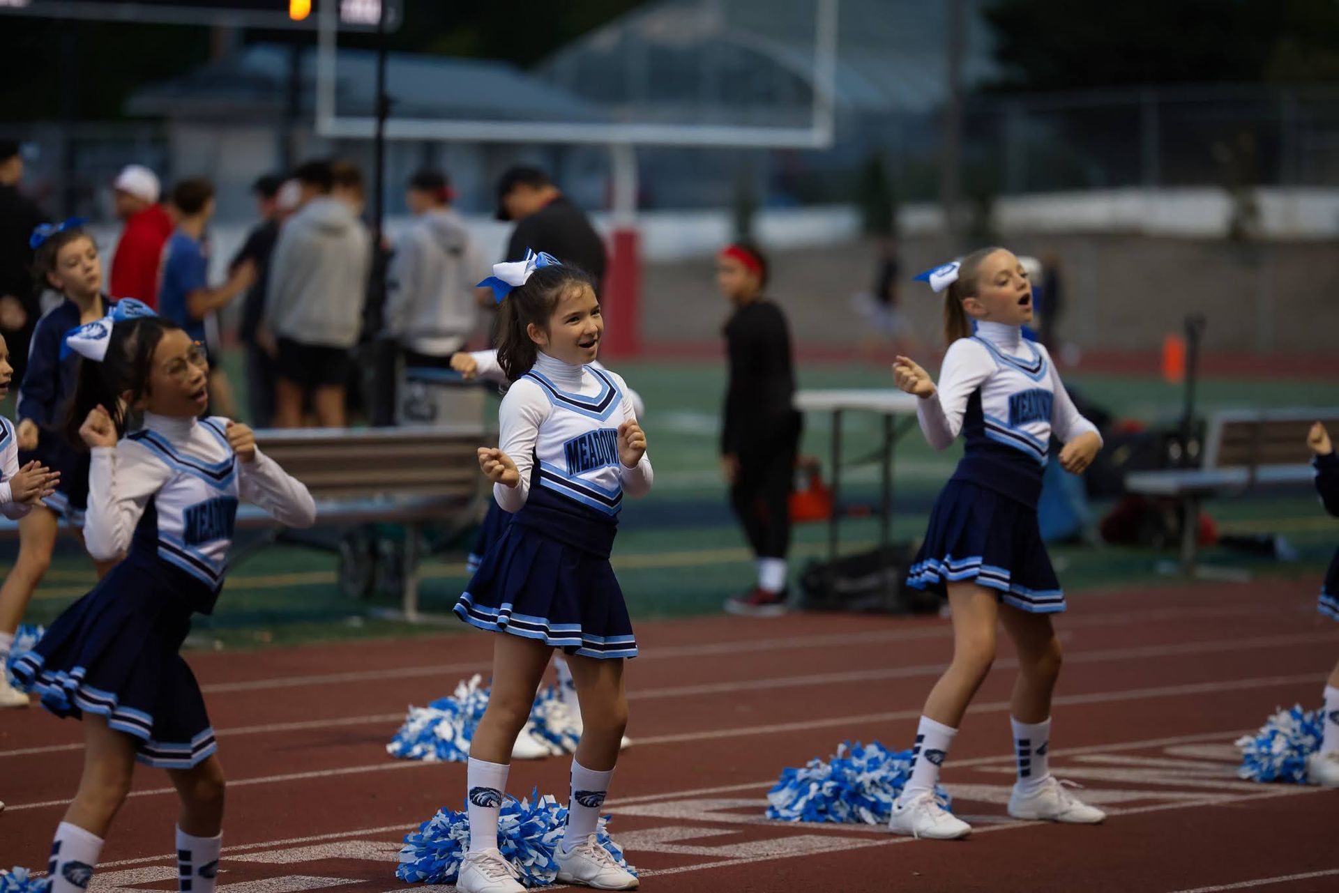 Cheerleaders in blue and white uniforms performing on a track with pom-poms at a stadium