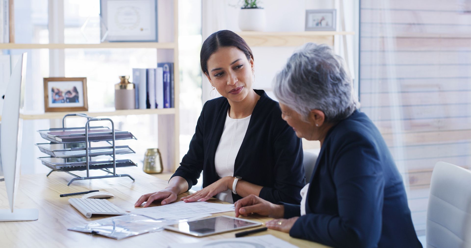 Two people reviewing documents together at a desk in a professional office setting. Two people reviewing documents together at a desk in a professional office setting.