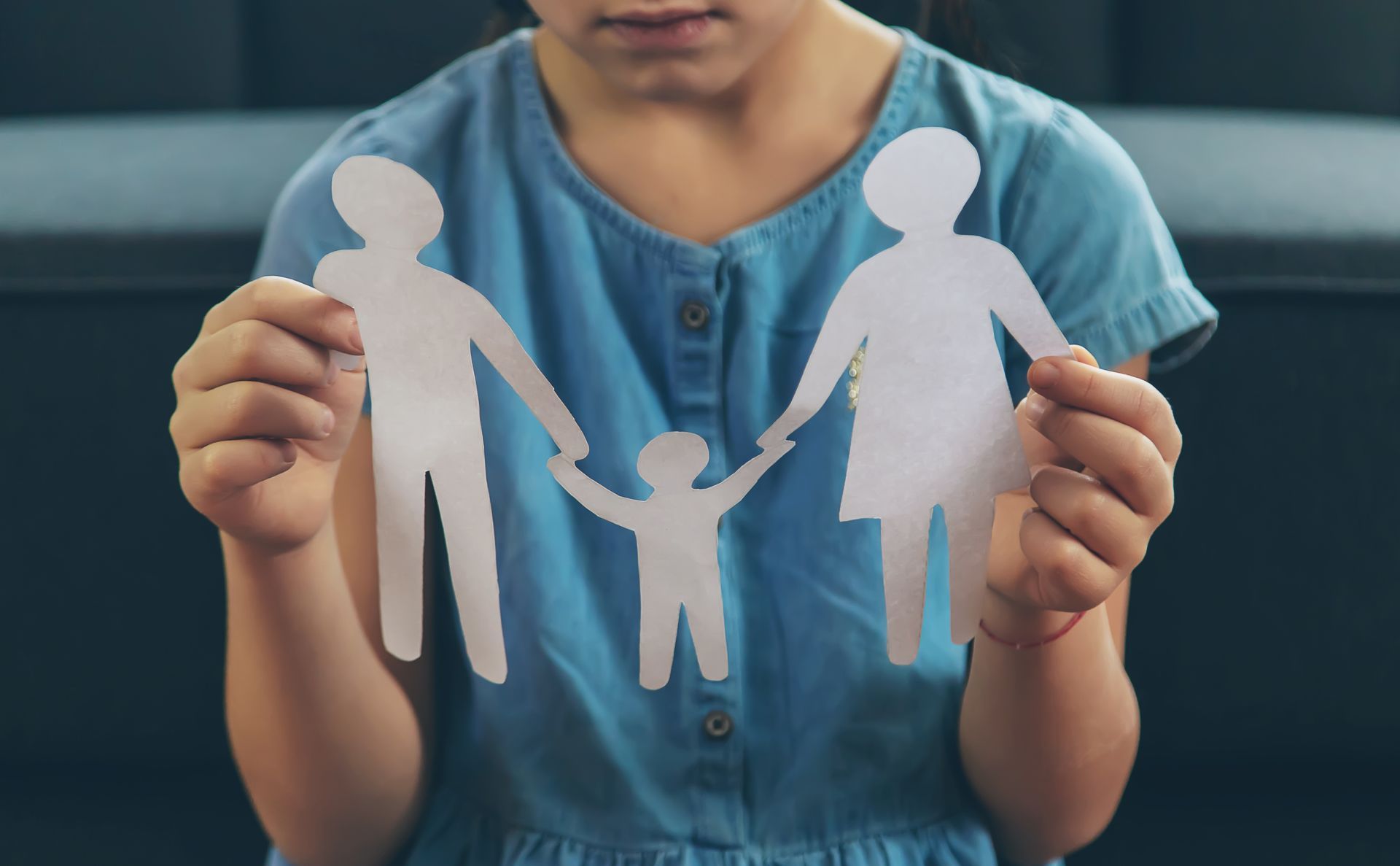A person in a blue shirt holds a white paper cutout of two adults holding hands with a child.