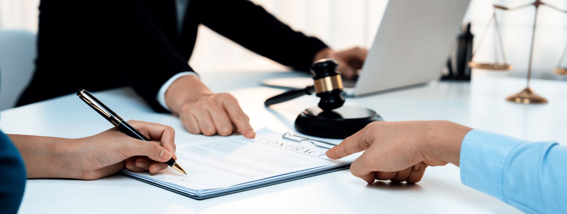 A divorce attorney reviews and signs legal documents with a client at an office desk. A divorce attorney reviews and signs legal documents with a client at an office desk.