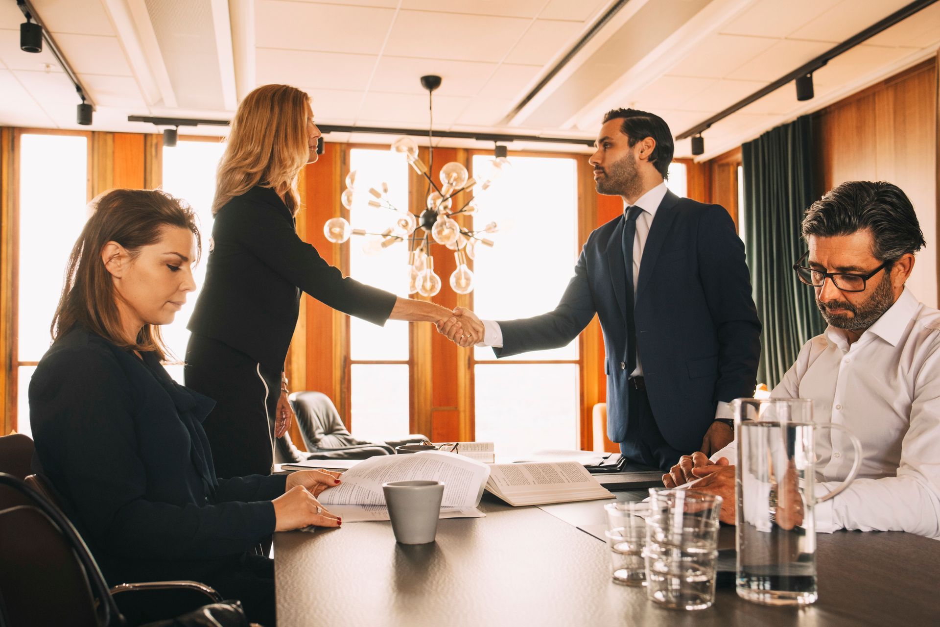 Divorce lawyers are shaking hands, and their team is sitting at a table in a law office.