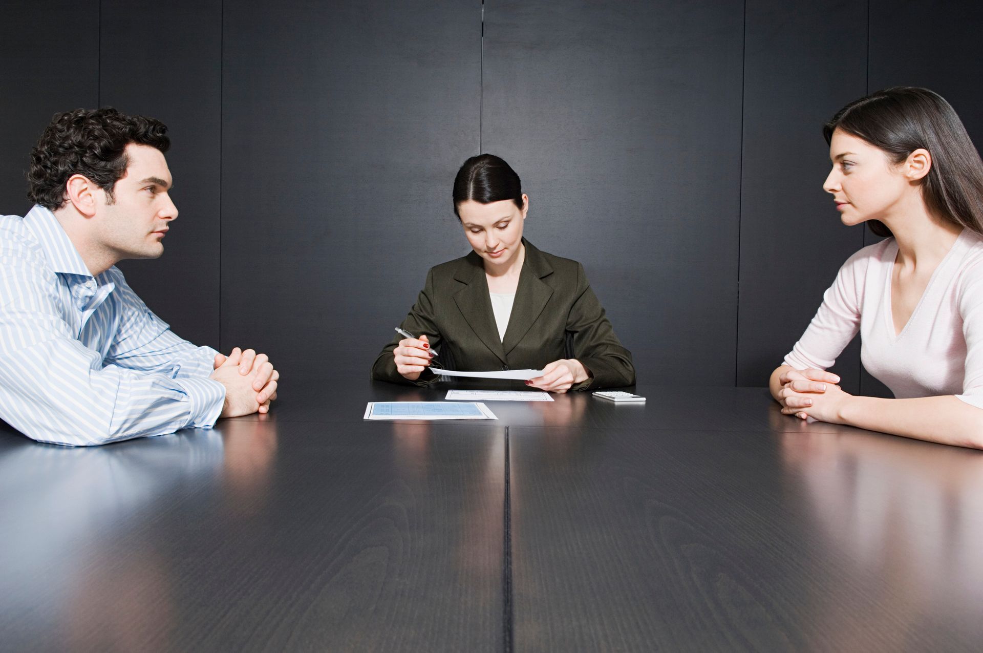 Three people in a meeting at a conference table with documents.