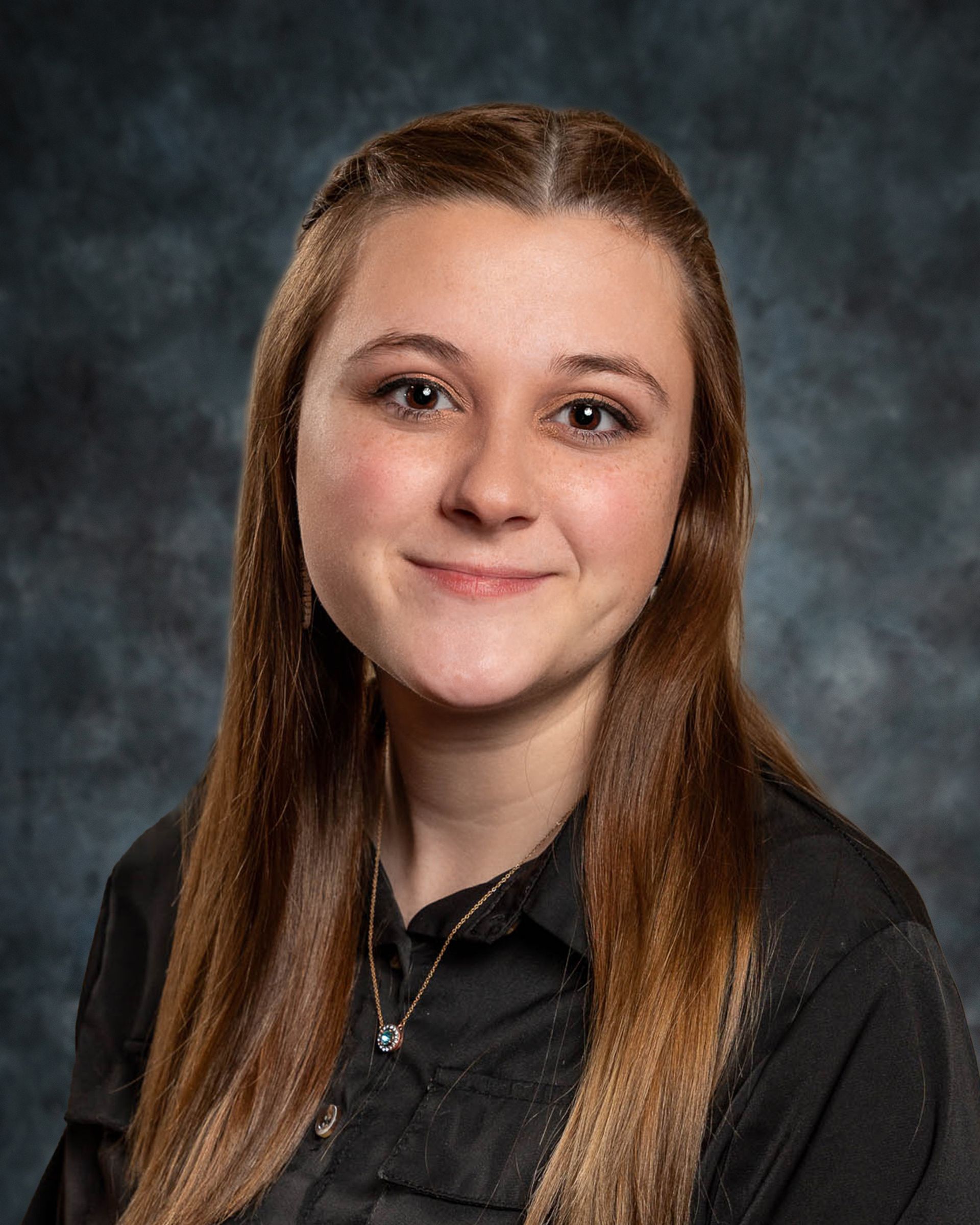 Young woman with long brown hair smiles, wearing a black shirt, against a dark blue background.