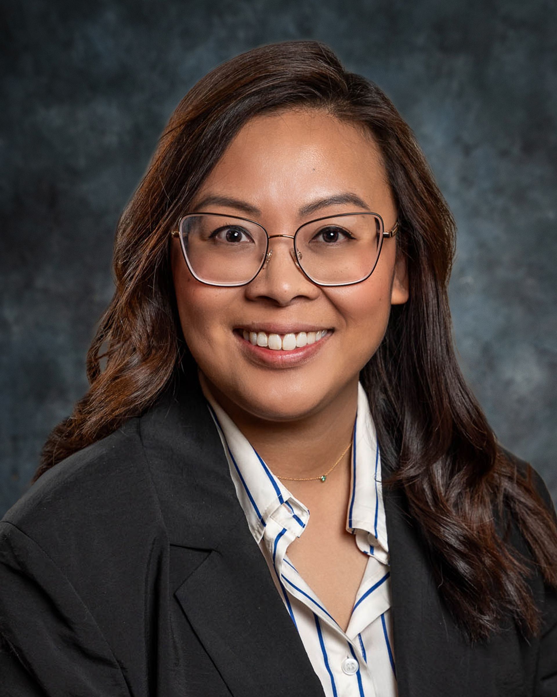 Woman wearing glasses, a black blazer, and striped shirt, smiling at the camera.