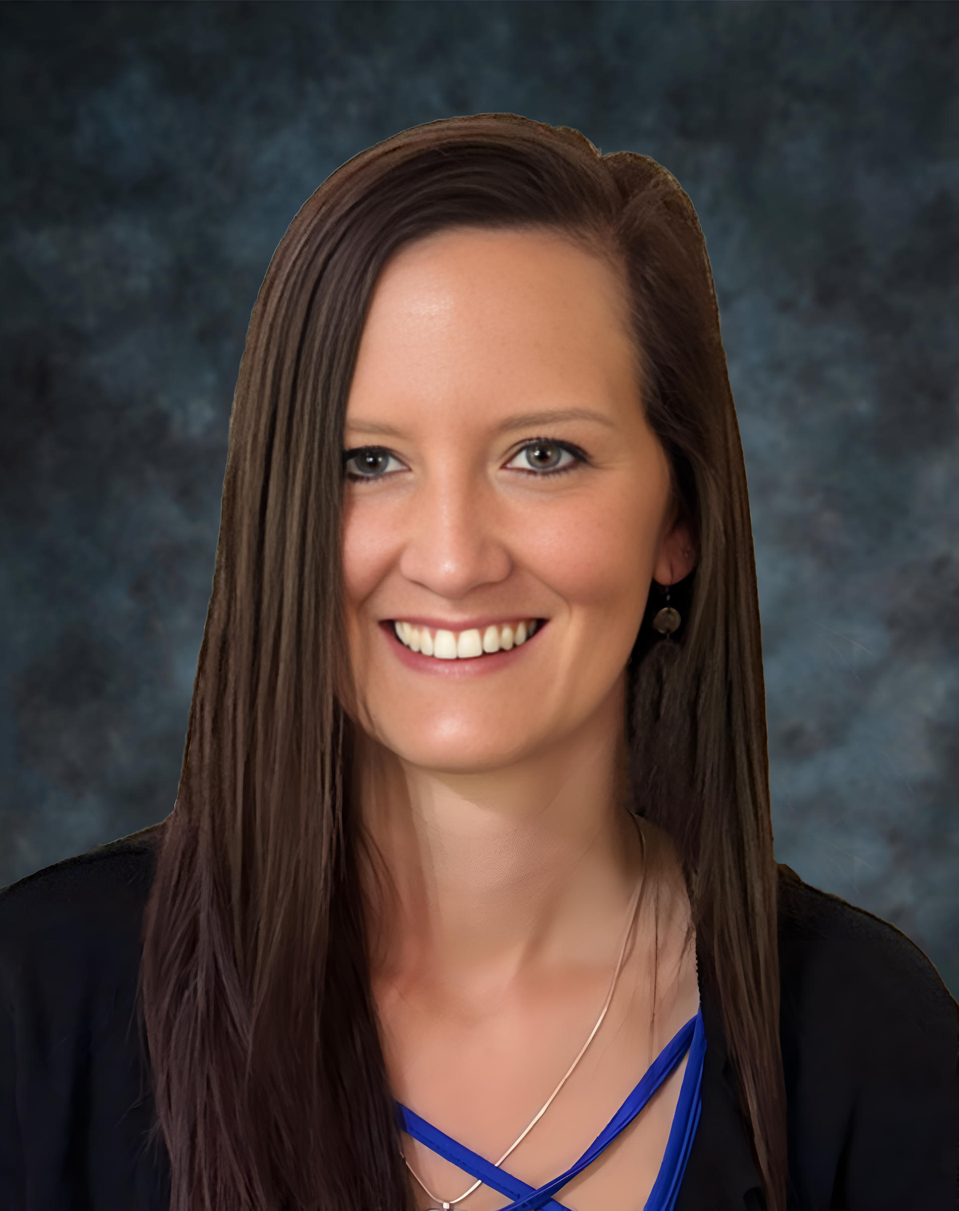 Woman with long brown hair smiling at the camera, wearing black and blue clothing against a dark background.