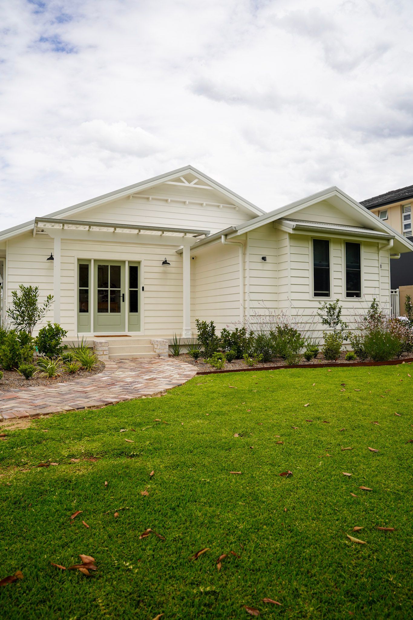 White house with a green door, surrounded by a lawn and a brick pathway.
