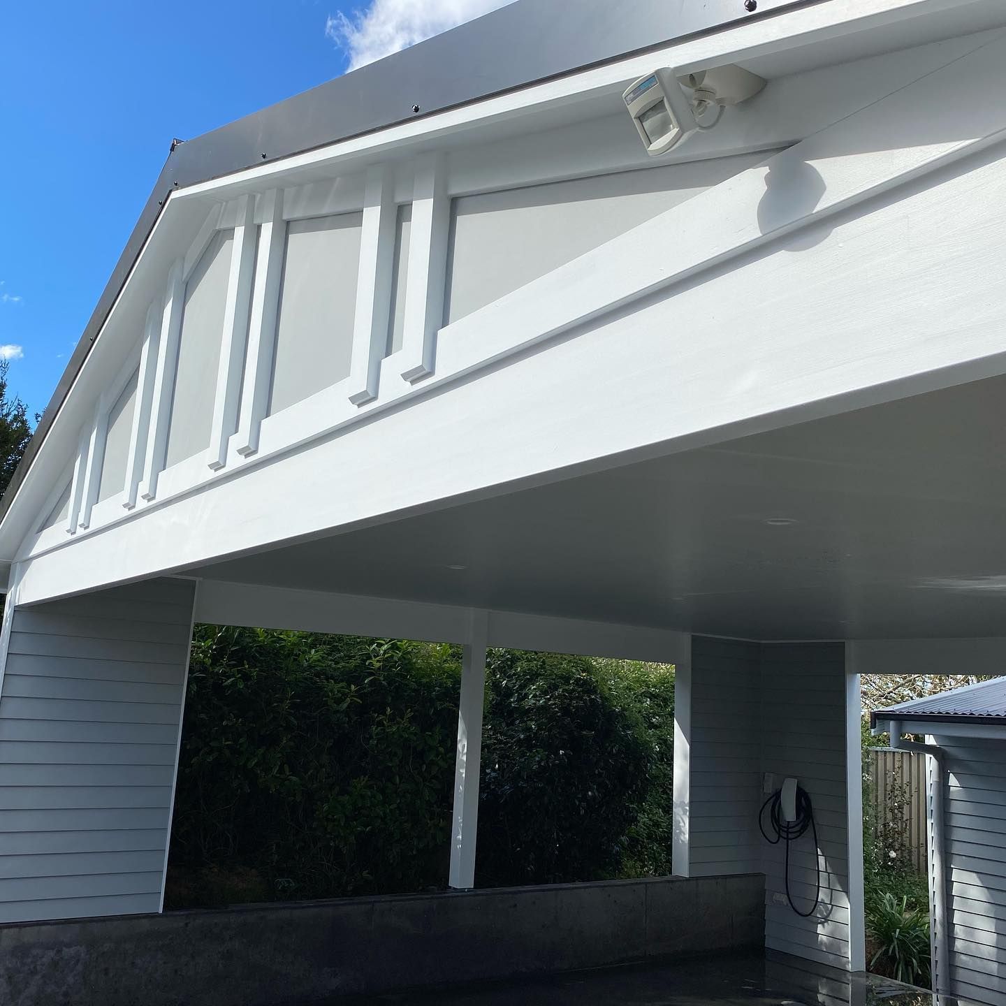 White carport with geometric design details, set against a blue sky, with a dark green hedge visible.