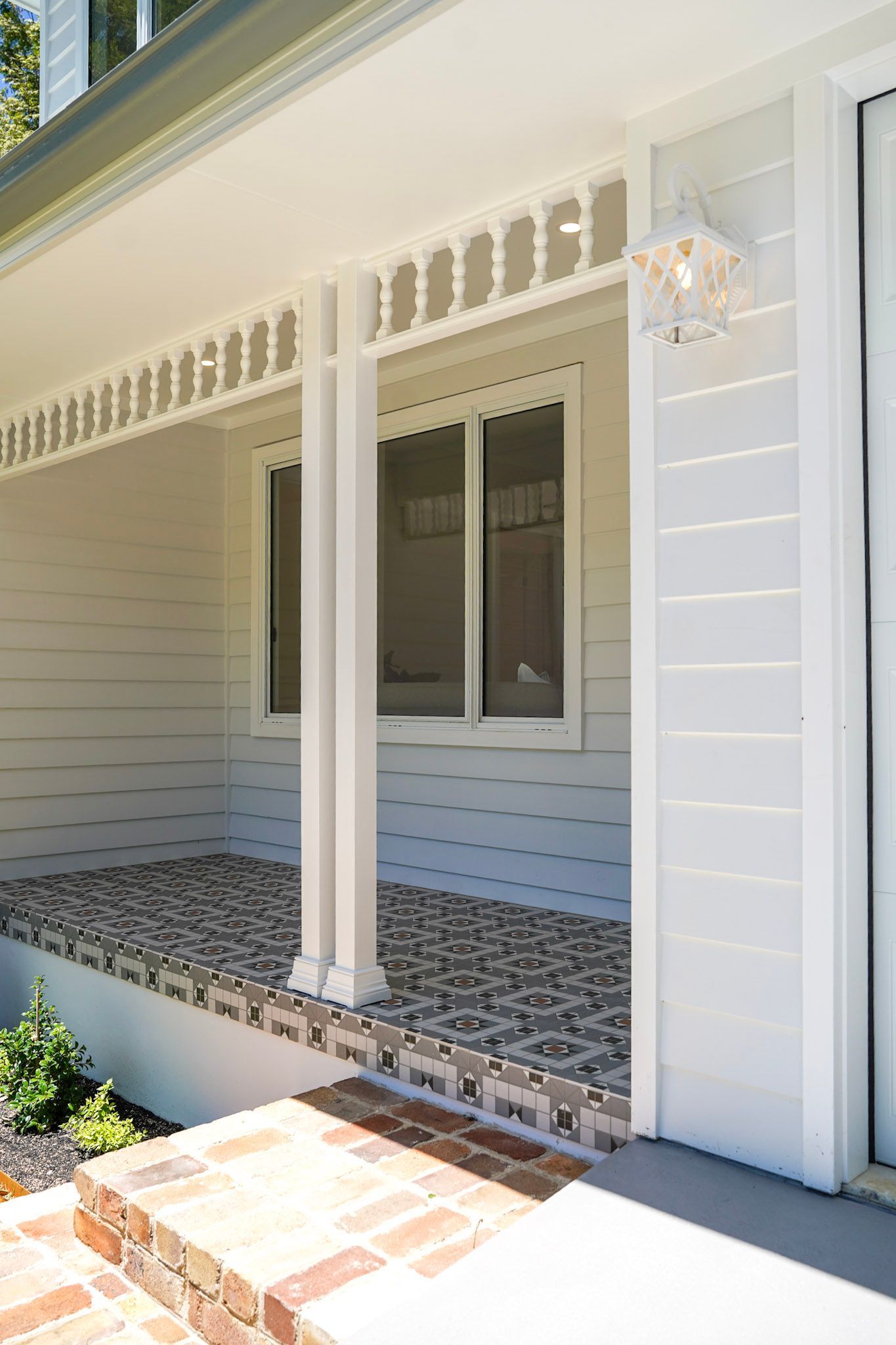Covered porch with white columns, patterned flooring, and a window. Brick steps lead to the porch.