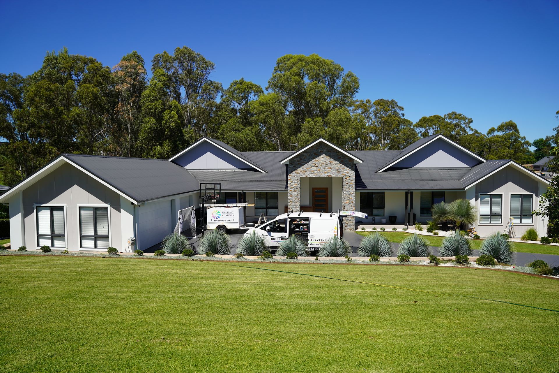 Large house with gray roof, stone facade, and green lawn; white utility truck parked in front.
