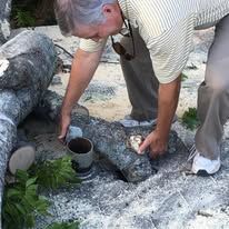 Person placing hands into a cylinder among large rocks outdoors, near a car
