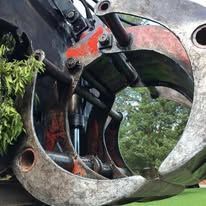 Close-up of a large weathered metal sculpture with circular openings and red paint, set outdoors on grass.