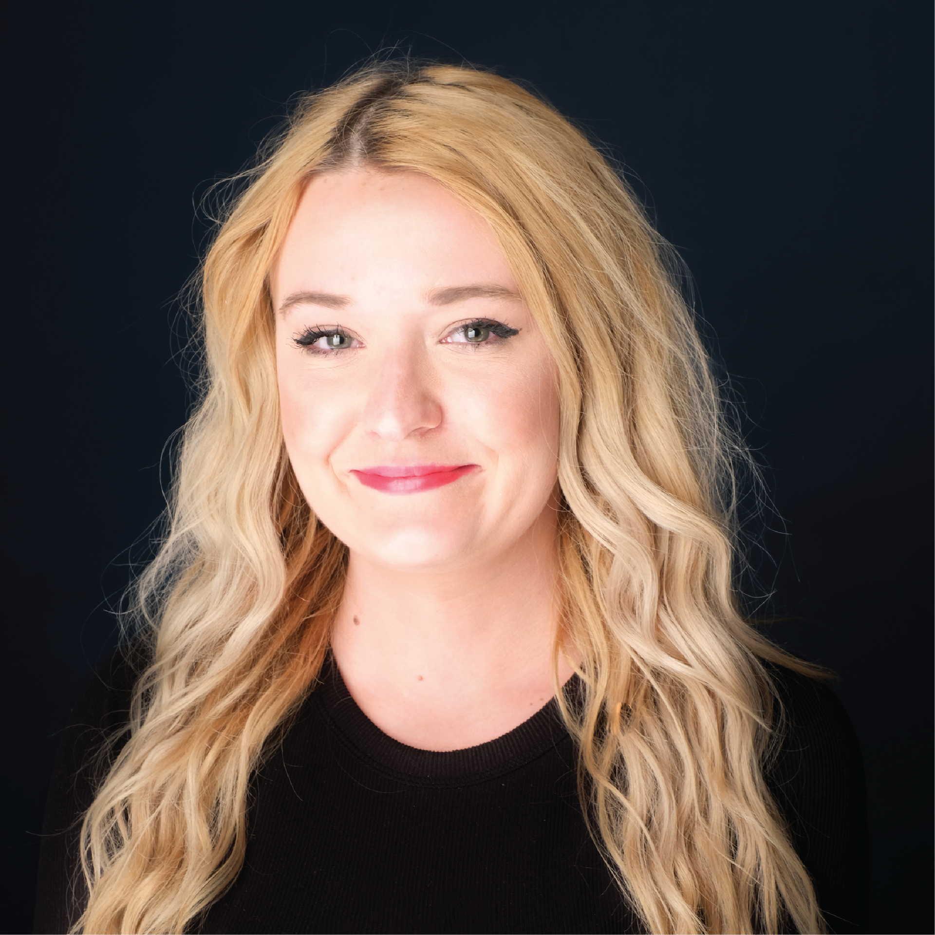 Portrait of a smiling blonde person in glasses against a blue studio backdrop