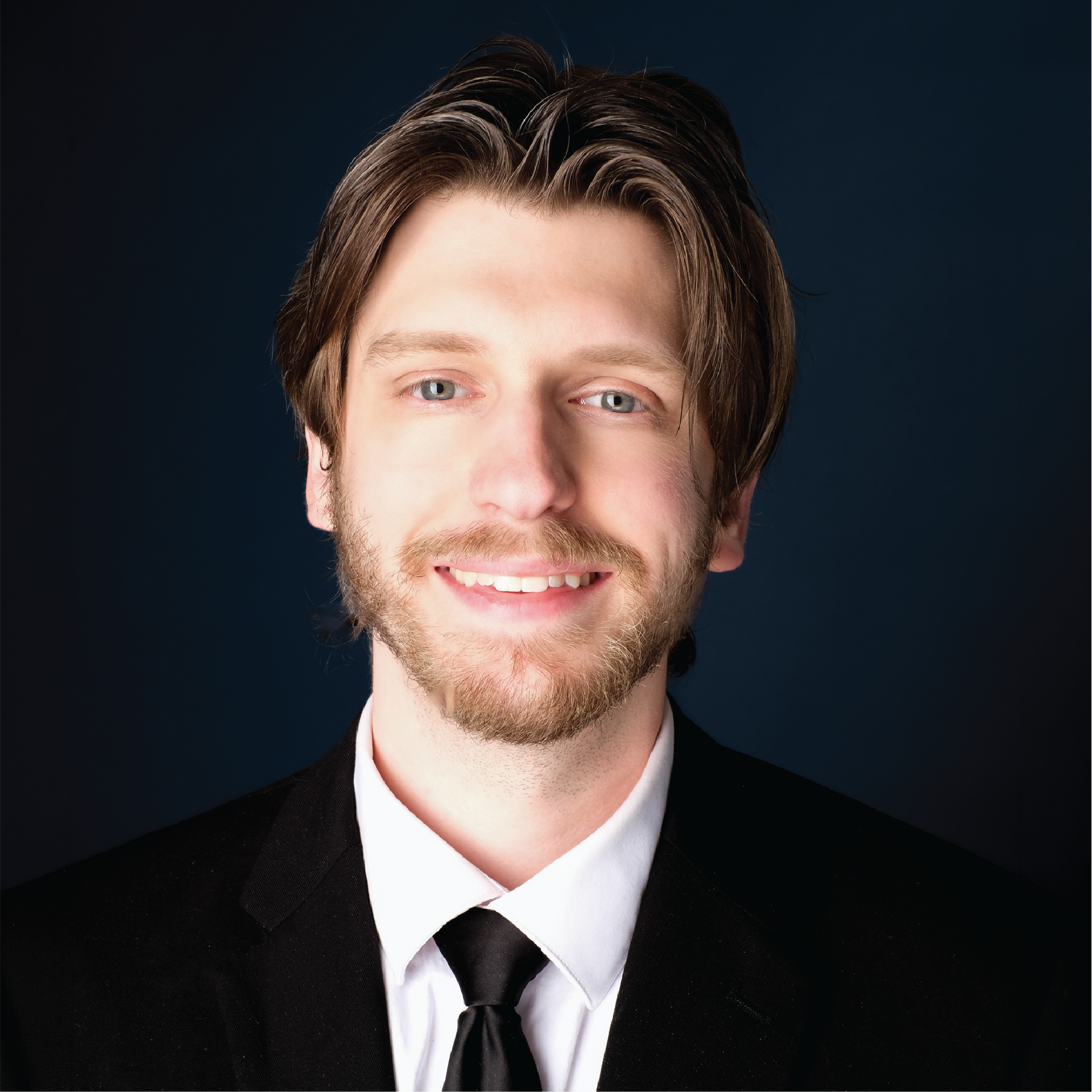 Smiling person in a white shirt and black tie against a gray studio backdrop