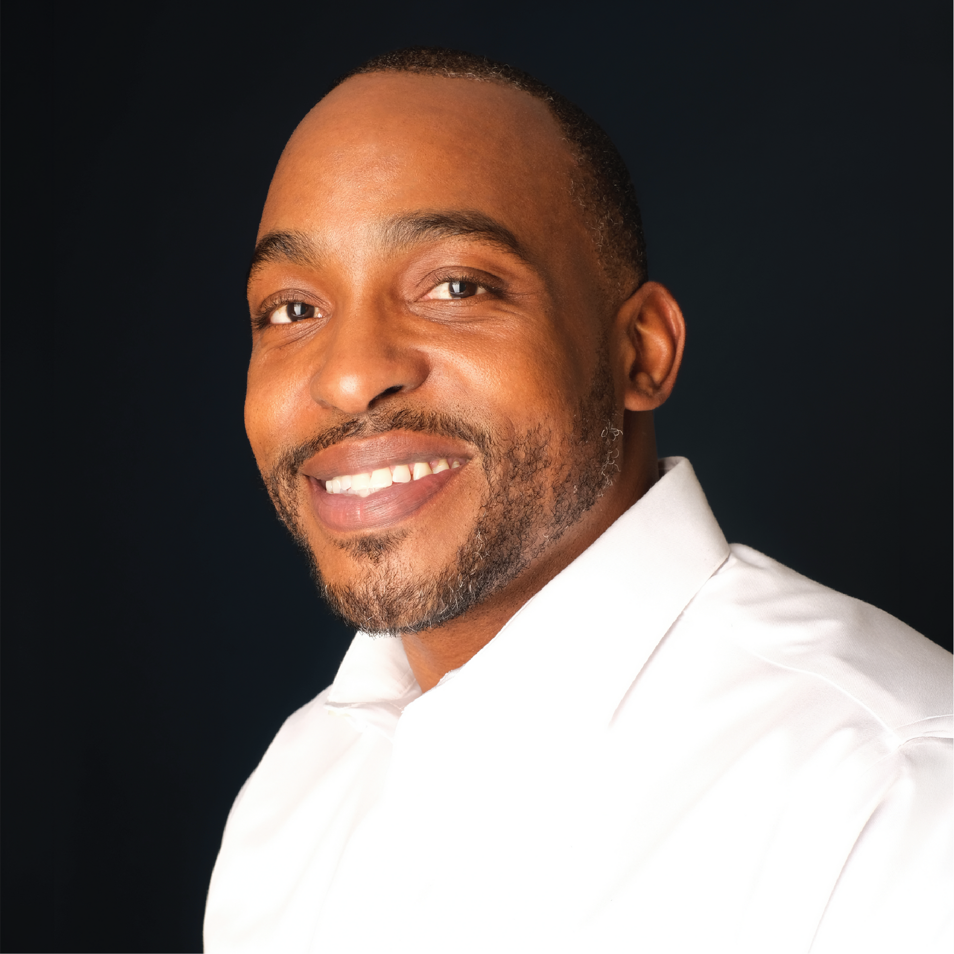 Smiling man in a black suit and white shirt against a blue studio backdrop