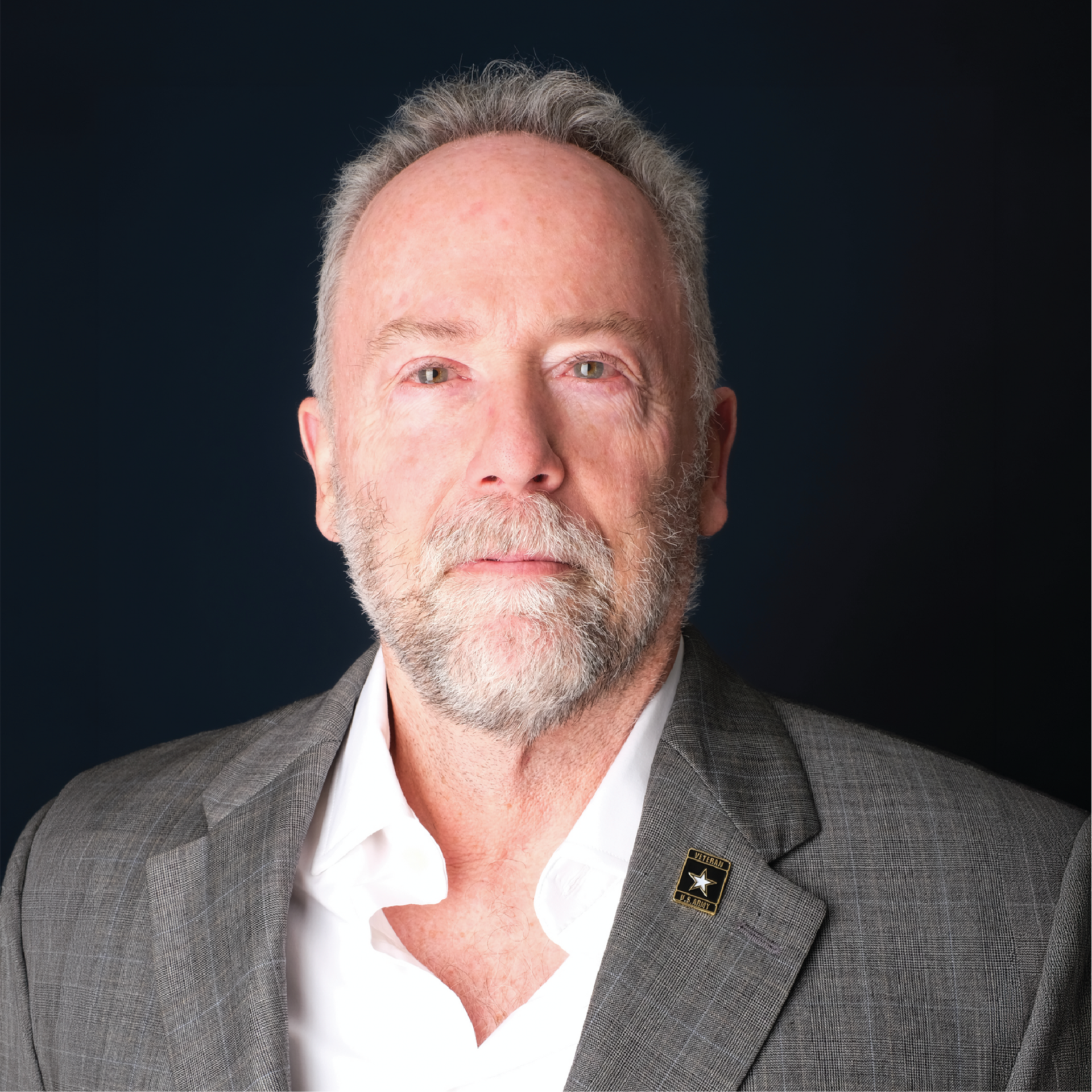 Portrait of a man in a gray blazer and white shirt against a blue studio backdrop