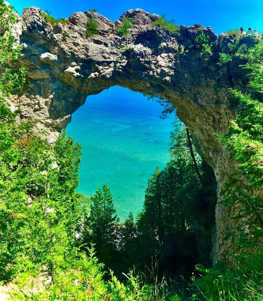 Natural rock arch framing turquoise water, green trees, and a bright blue sky