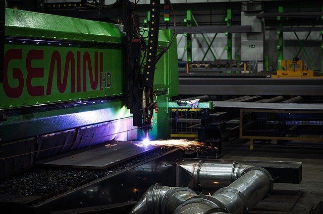 Large green industrial cutting machine sparks over metal pipes in a factory setting