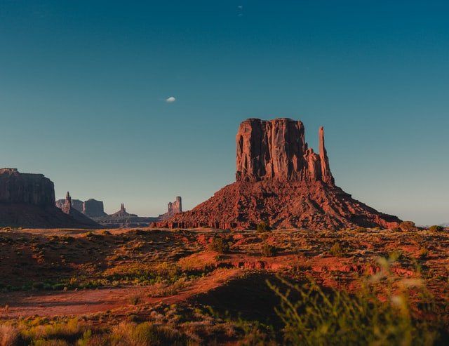 Sunlit red sandstone butte in a desert landscape under a clear blue sky