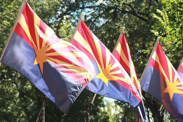 Three Arizona state flags waving against a leafy outdoor background.