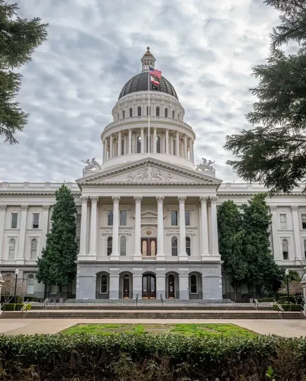 White neoclassical capitol building with dome and columns, framed by trees under a cloudy sky