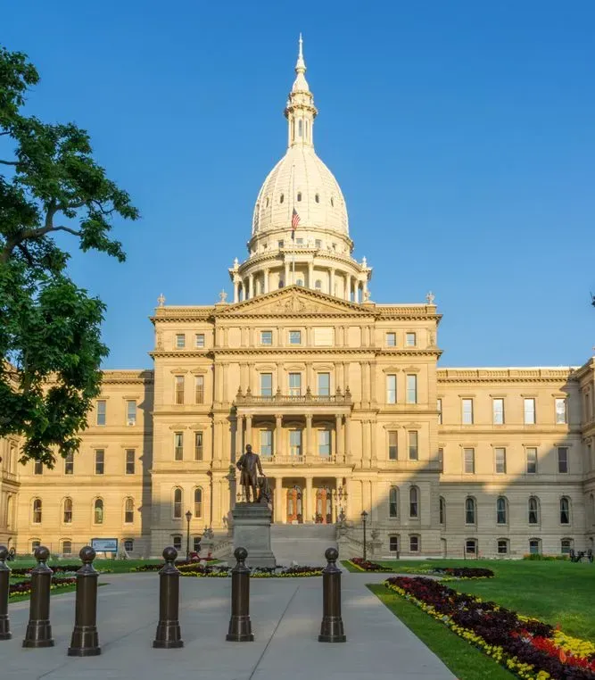 Large historic capitol building with a white dome, viewed from a formal garden under a clear blue sky
