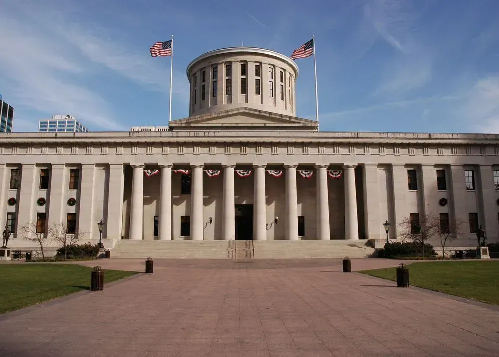 Ohio Statehouse with white columns and central rotunda, viewed from the front under a clear sky.