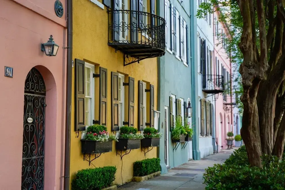 Colorful pastel row houses with balconies and potted plants along a tree-lined sidewalk