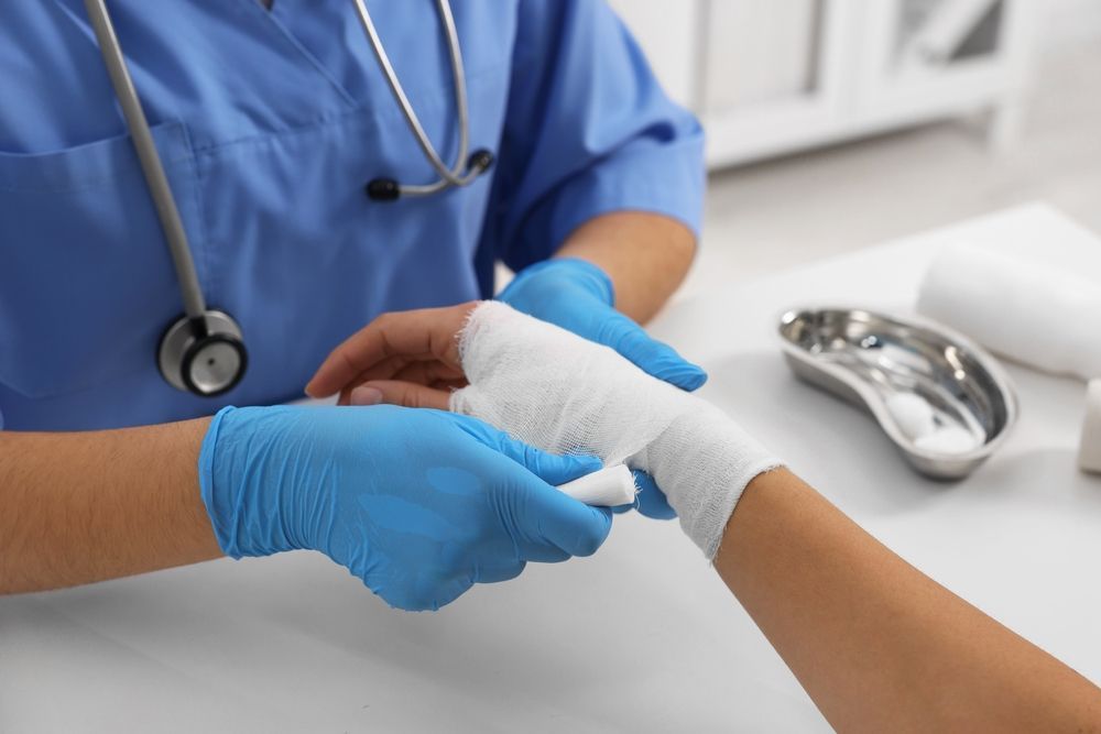 Healthcare worker bandaging a patient’s wrist with white gauze and blue gloves.