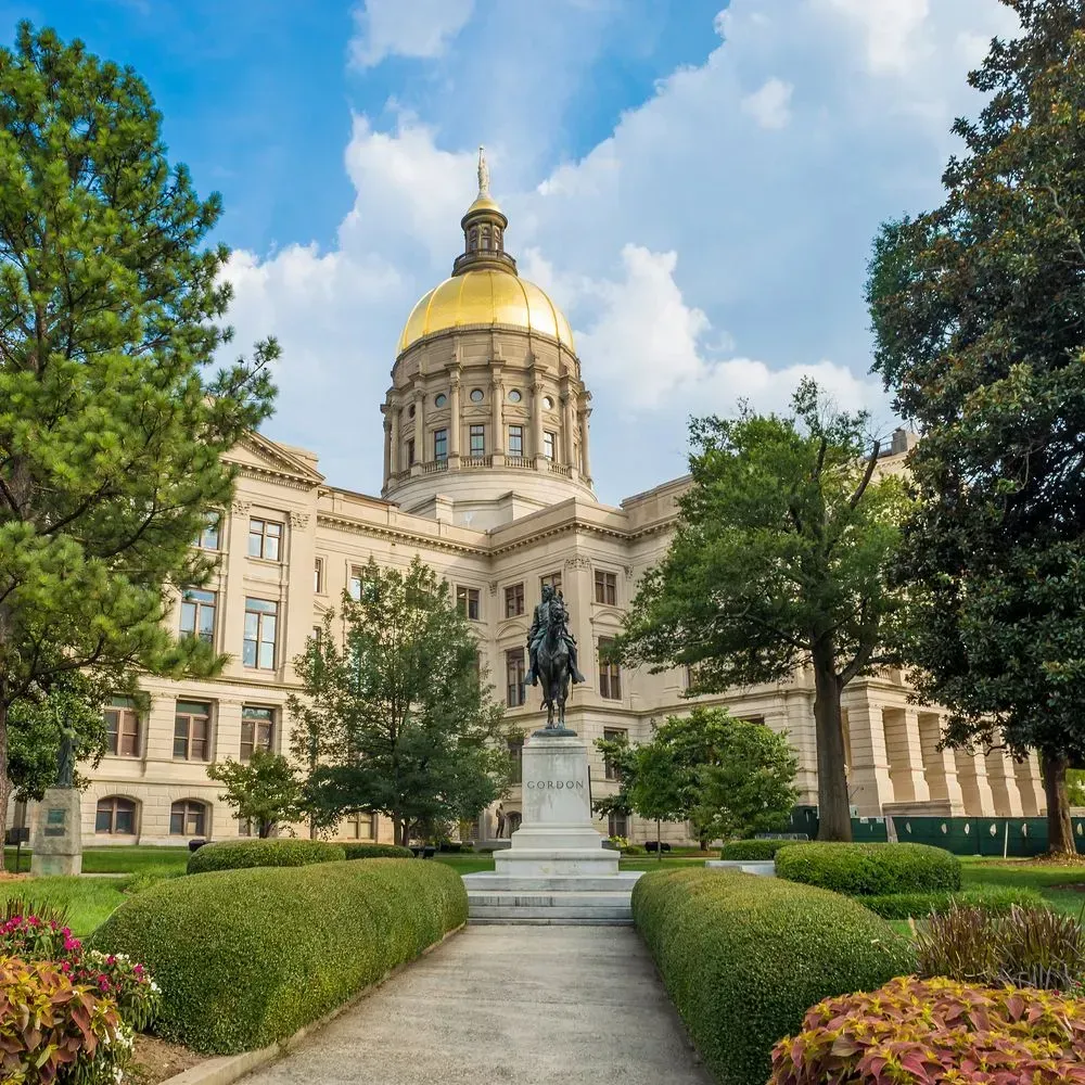 Georgia State Capitol with gold dome, statue, and landscaped gardens under a blue sky