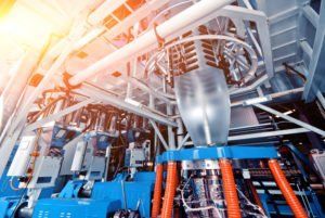 Industrial machinery in a factory, with metal pipes, blue equipment, and bright orange lighting.