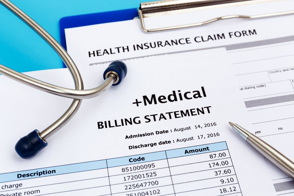 Medical billing statement and health insurance claim form on a blue clipboard with stethoscope and pen.