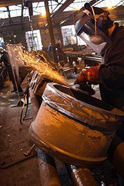 Worker grinding metal in an industrial shop, sending sparks from a large barrel.