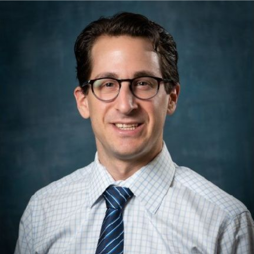 Smiling man in glasses and tie, posed against a blue studio background