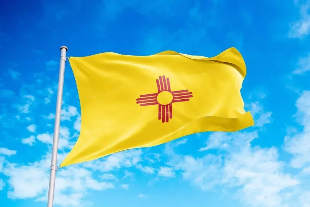 Yellow New Mexico state flag waving against a blue sky
