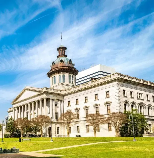 Historic neoclassical courthouse building with a central tower, white columns, and green lawn under a blue sky