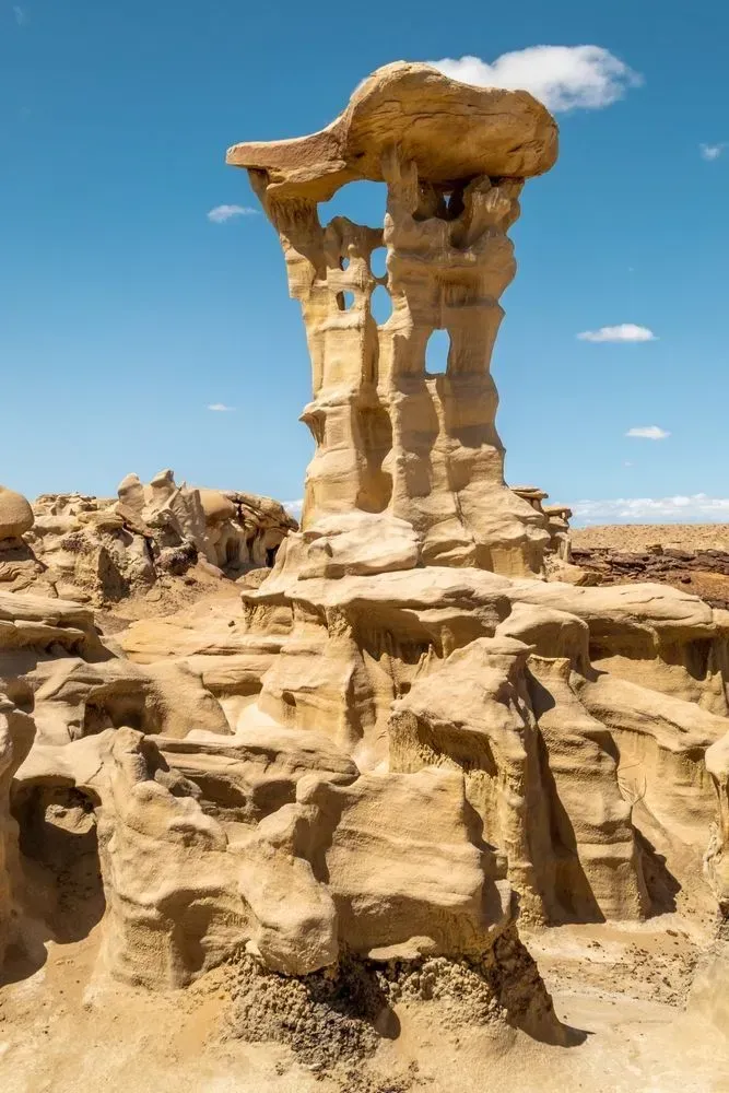 Desert rock formation with a tall sandstone pillar under a blue sky with clouds