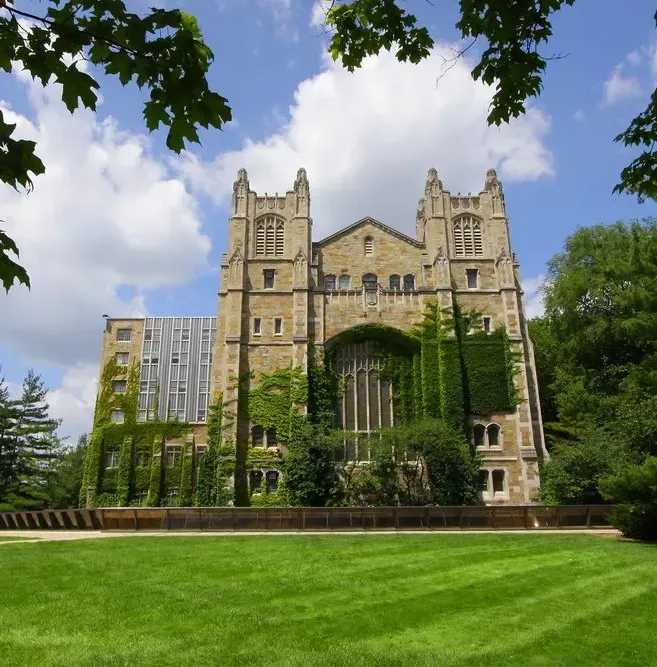 Historic stone building with ivy-covered facade beside a green lawn under a blue sky.