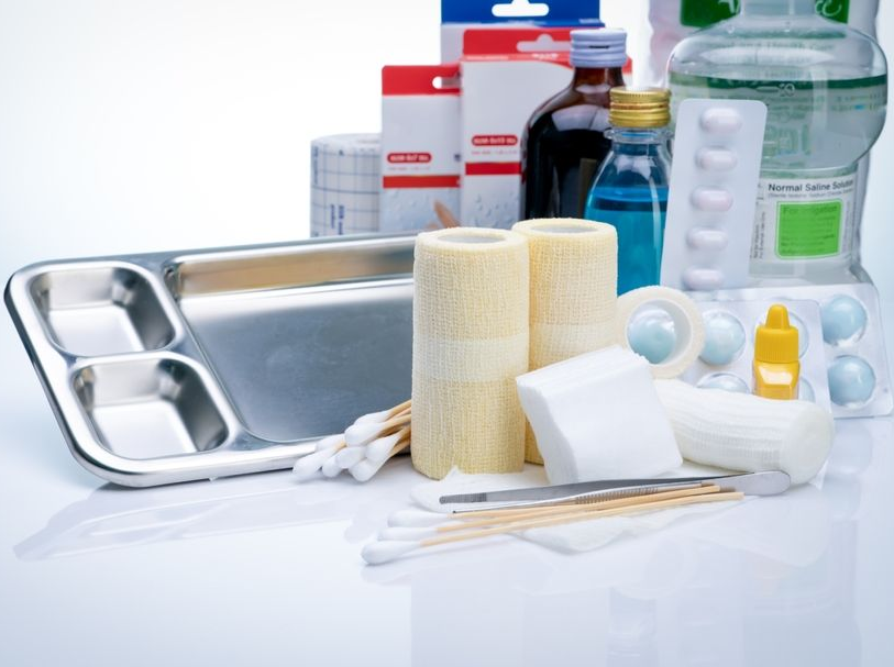 First aid and medical supplies arranged on a tray, including bandages, gauze, bottles, and a stethoscope.