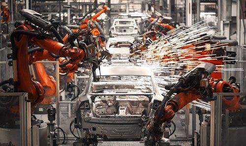 Robotic arms welding car bodies on an assembly line, sparks flying in a factory