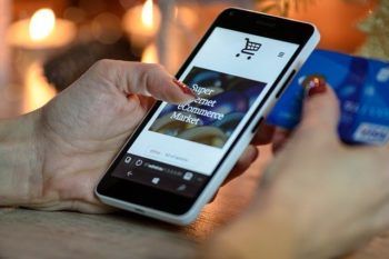 Hands holding a smartphone with a shopping app while swiping a credit card
