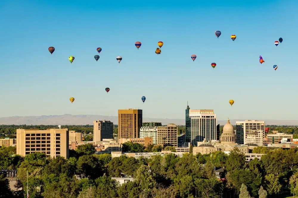 Colorful hot air balloons float over a city skyline on a clear blue morning.