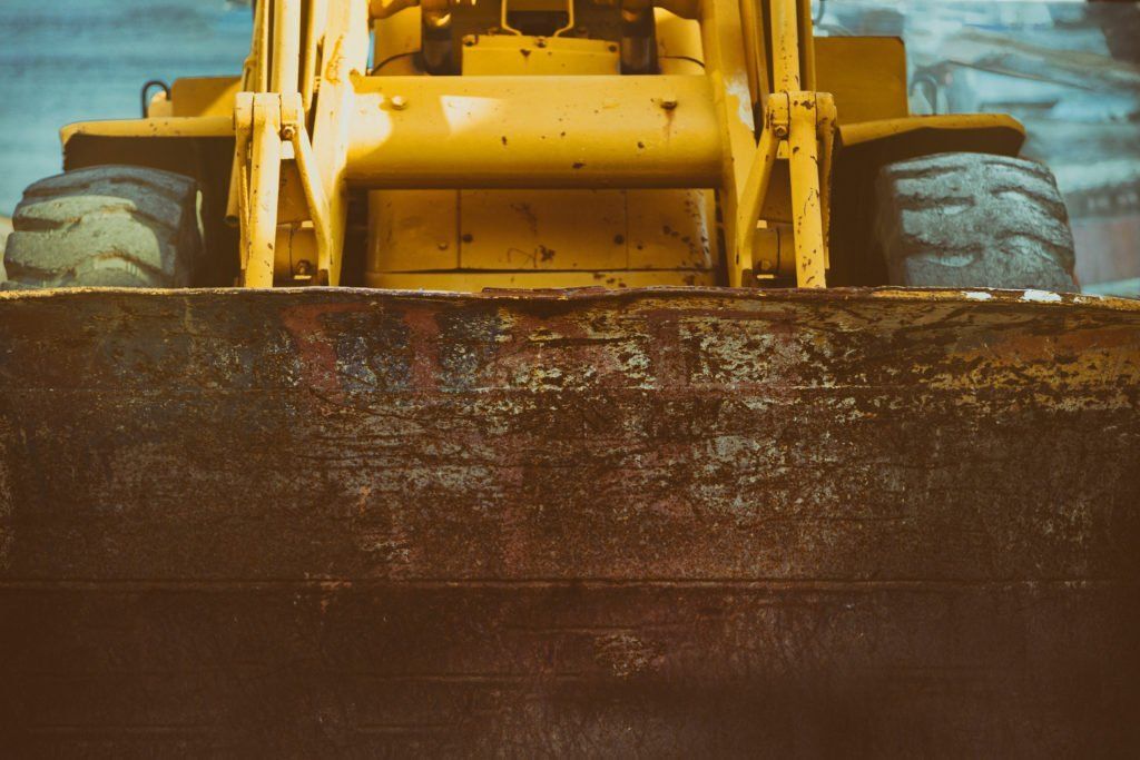 Yellow bulldozer pushing a mound of dark soil, front view at a construction site