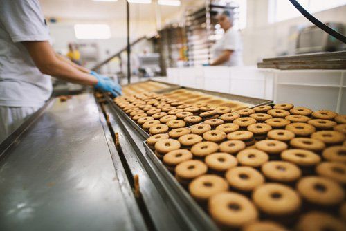 Worker in a bakery handling a conveyor belt of freshly baked donuts