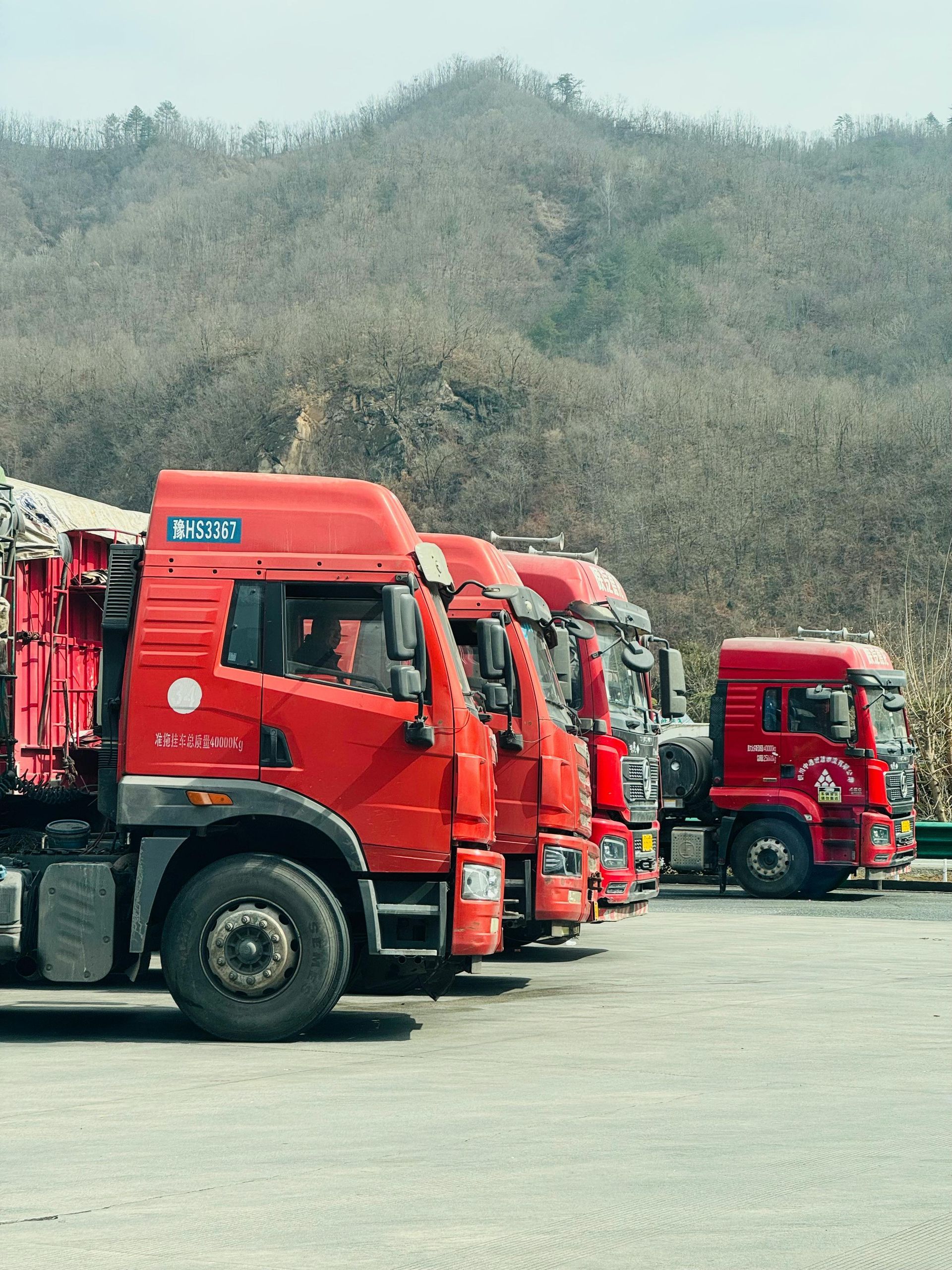 Red cargo trucks parked in a row on a lot with hills in the background