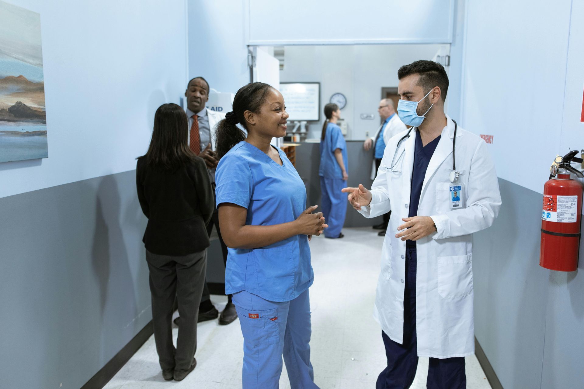 Doctor and nurse talking in a hospital hallway, with another staff member in the background.
