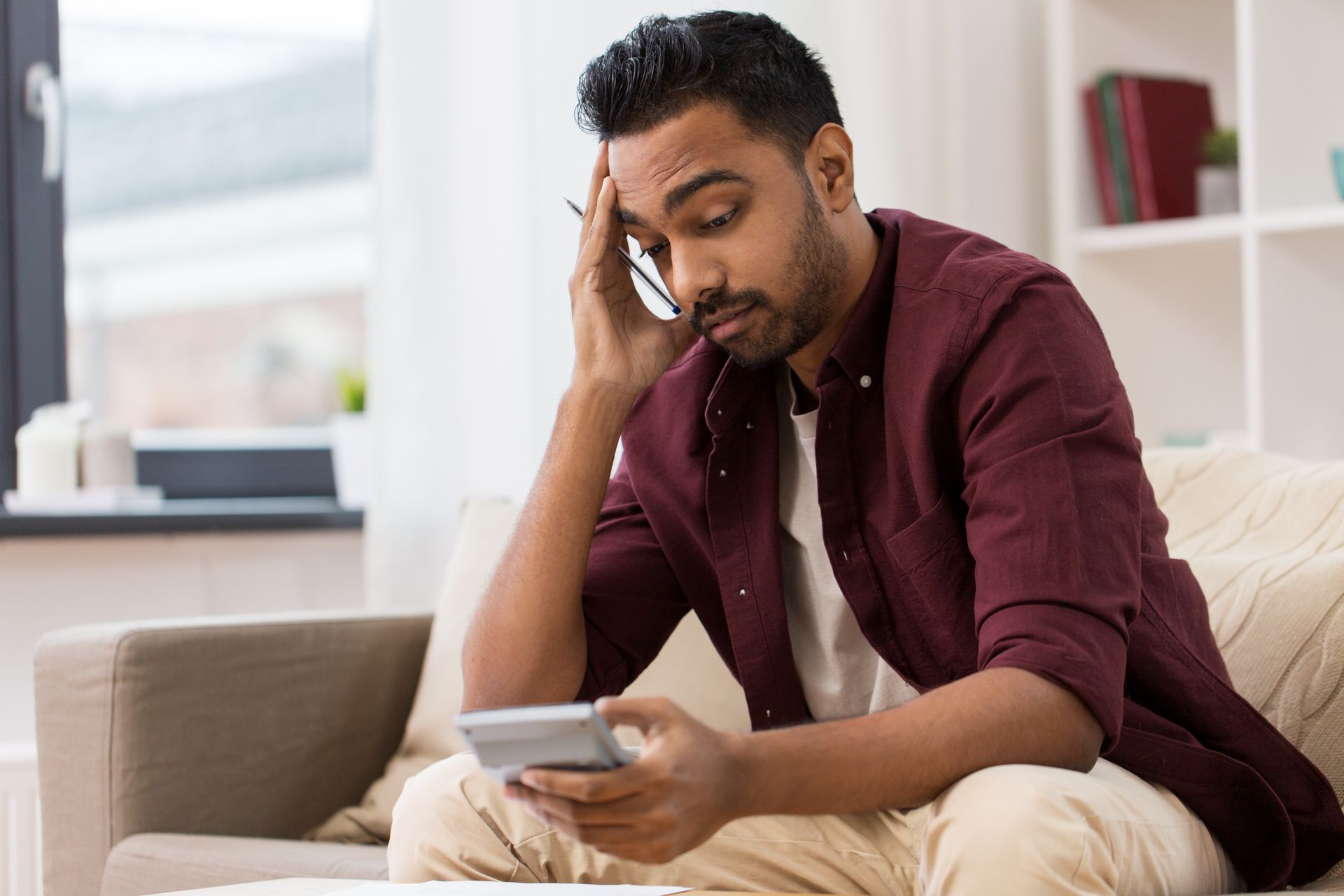 Man sitting on a couch, holding his head and looking stressed while reading a phone screen